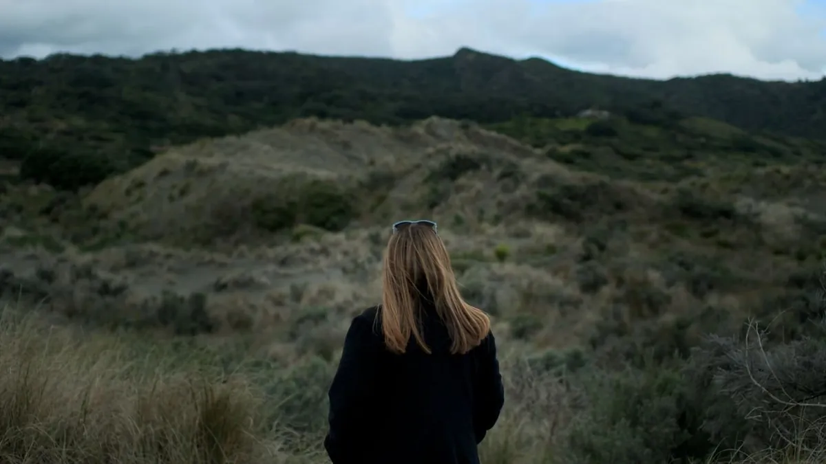A woman with sunglasses resting on her head looks out across rolling hills.